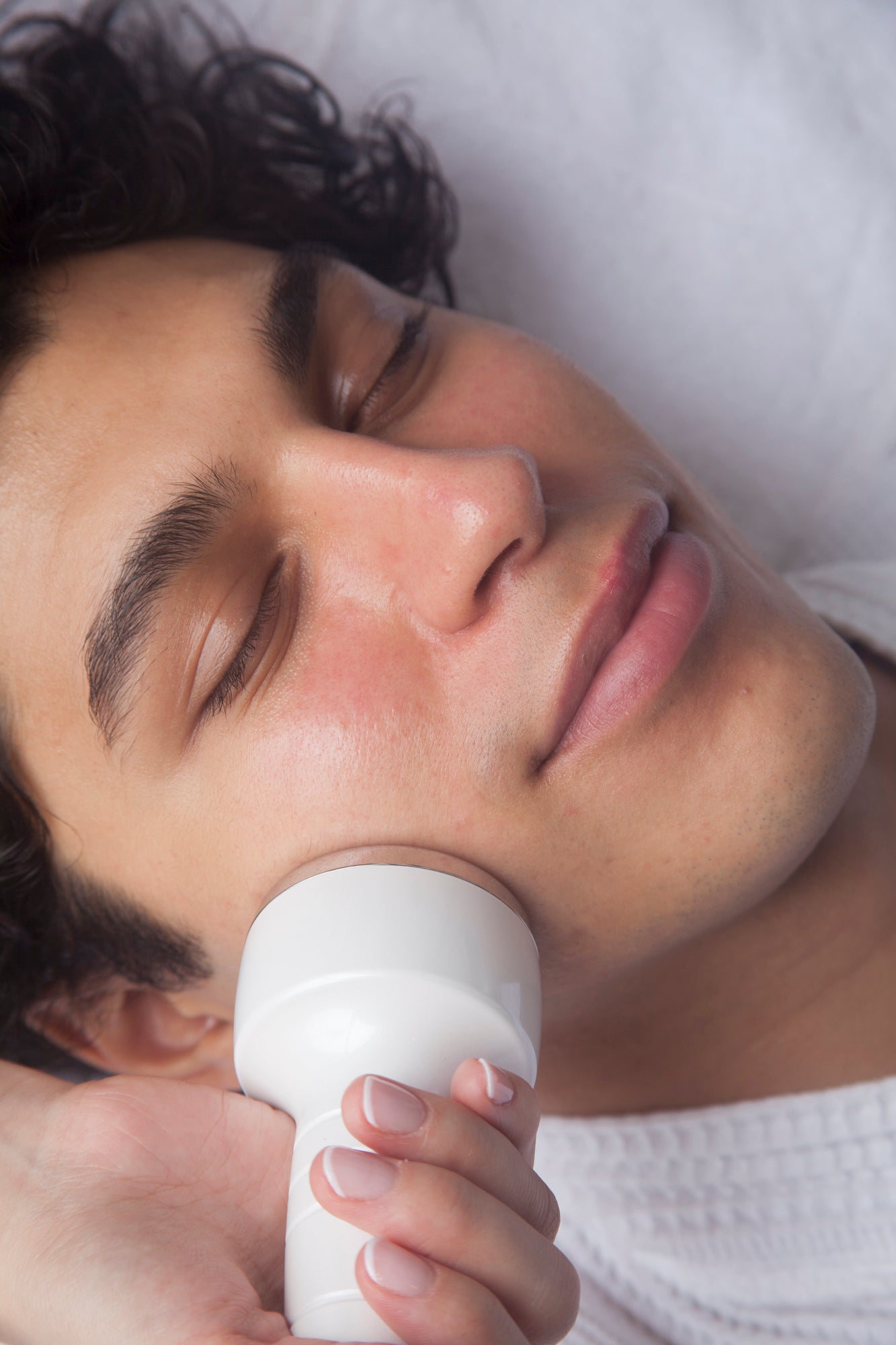 Man's face in profile with hand holding white facial cream jar against cheek.