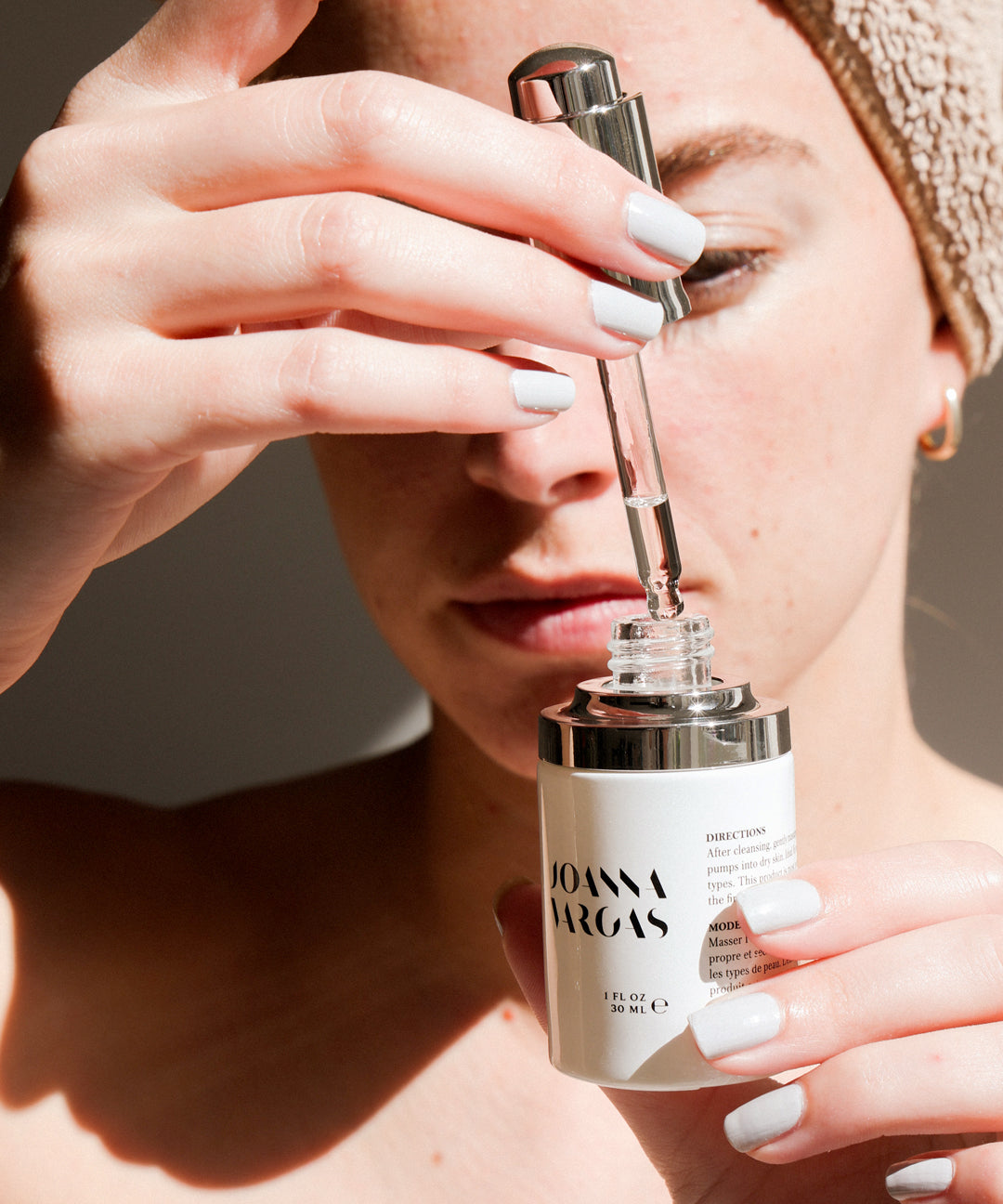 Person holding a glass dropper bottle of serum with a white label and rose gold cap.