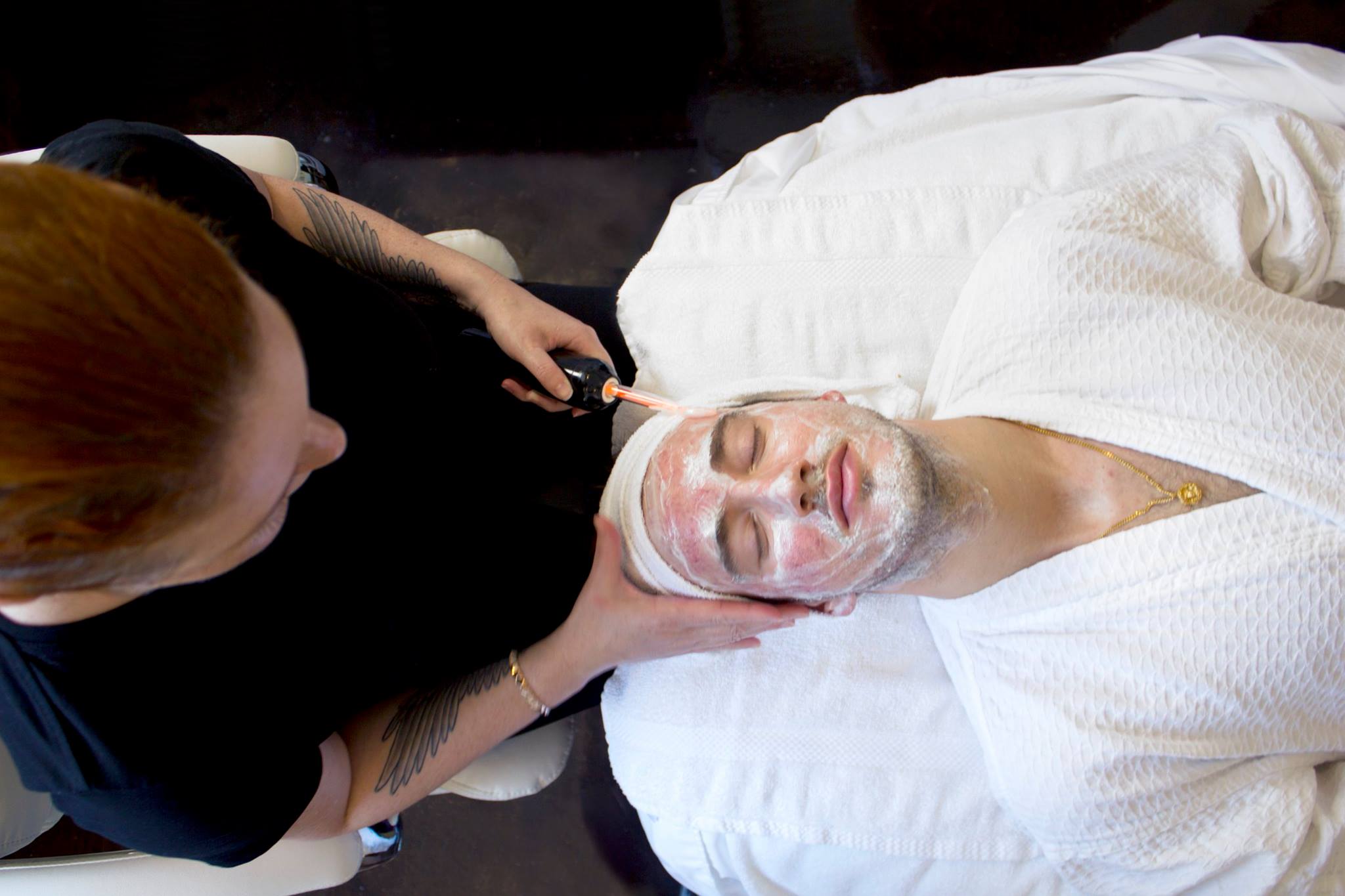 Man receiving facial treatment with cream mask applied to face while lying on white towel.